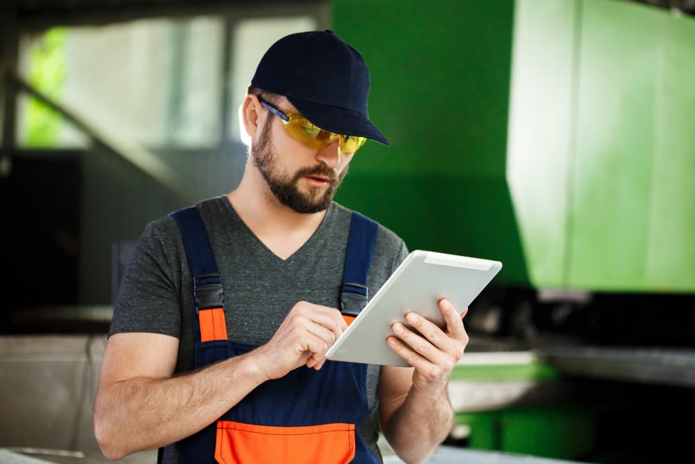 Ein Arbeiter mit Brille und Mütze hält ein Tablet.